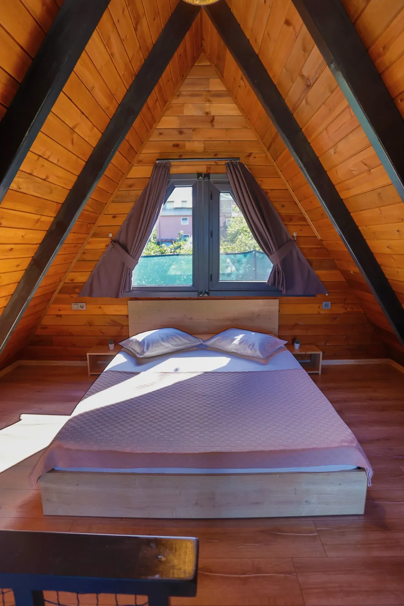 Ahşap A-frame çatının altında pencereye bakan çift kişilik yatak