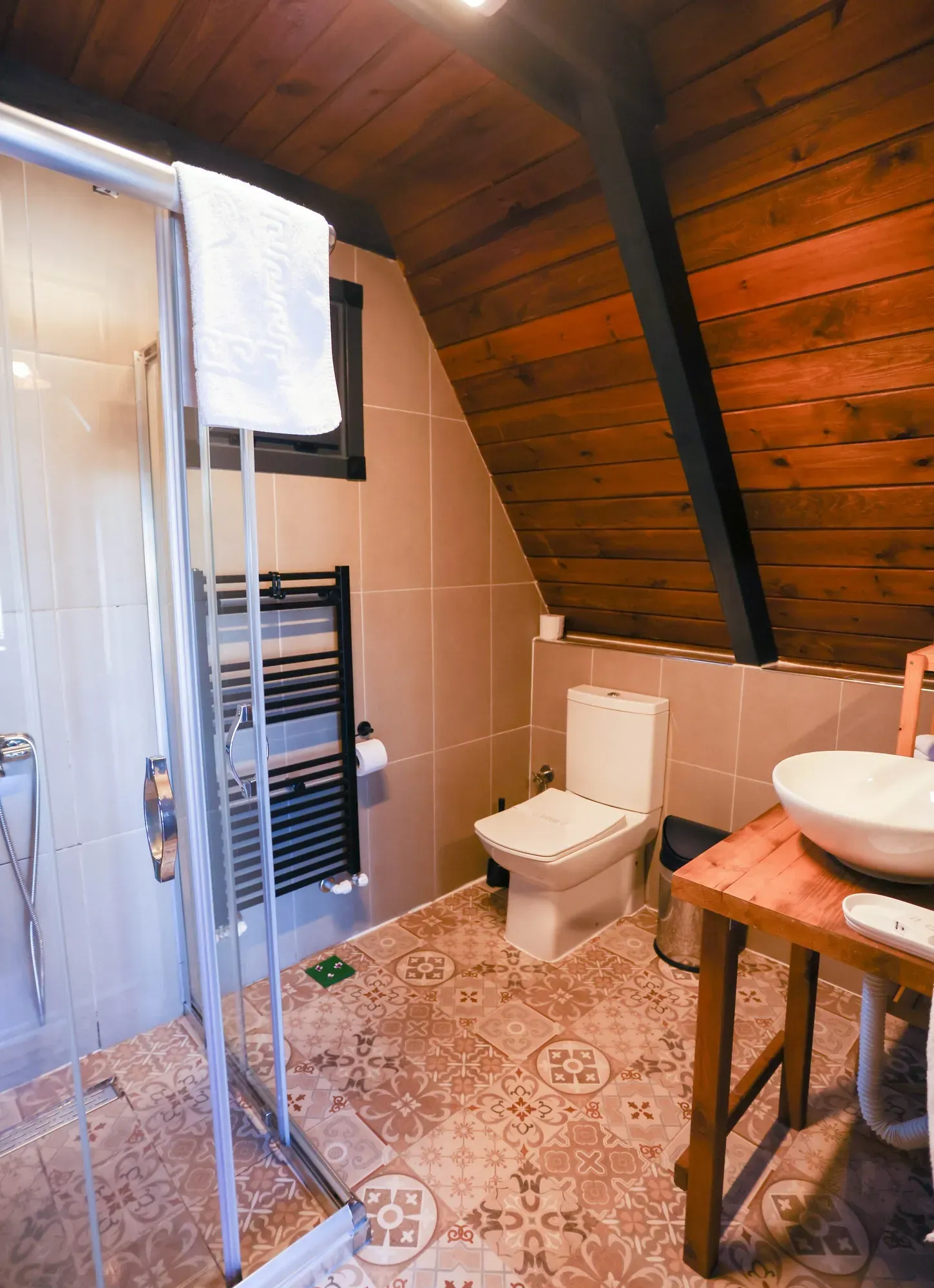 Ahşap çatılı banyo: duşakabin, havlupan, klozet ve ahşap tezgahta lavabo