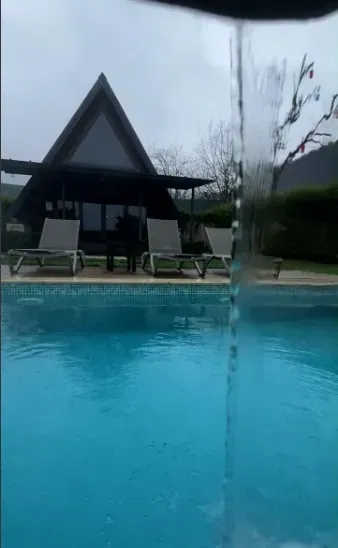 Yağmurlu bir günde havuza dökülen çelik şelale, arkada A-frame bungalov