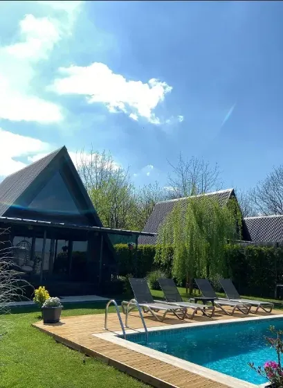Mavi gökyüzü altında A-frame bungalov, ahşap güverte, şezlonglar ve havuz